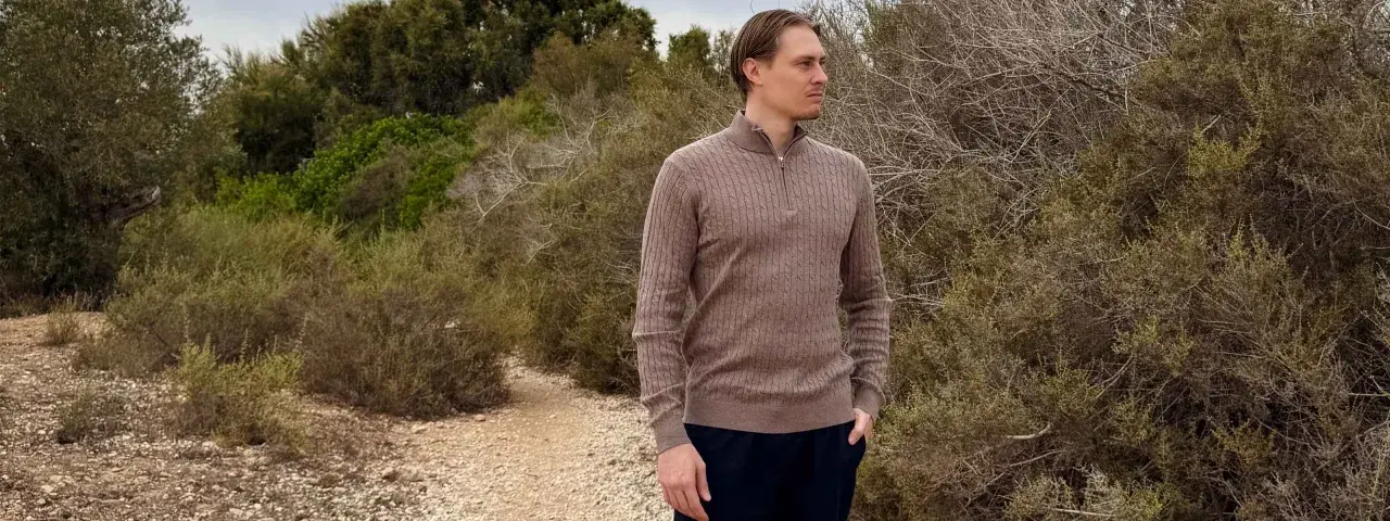 Mann in braunem Zopfmuster-Pullover aus Kaschmir, der in der Natur steht. Ist Kaschmir warm? Ja, dieser Pullover beweist es.