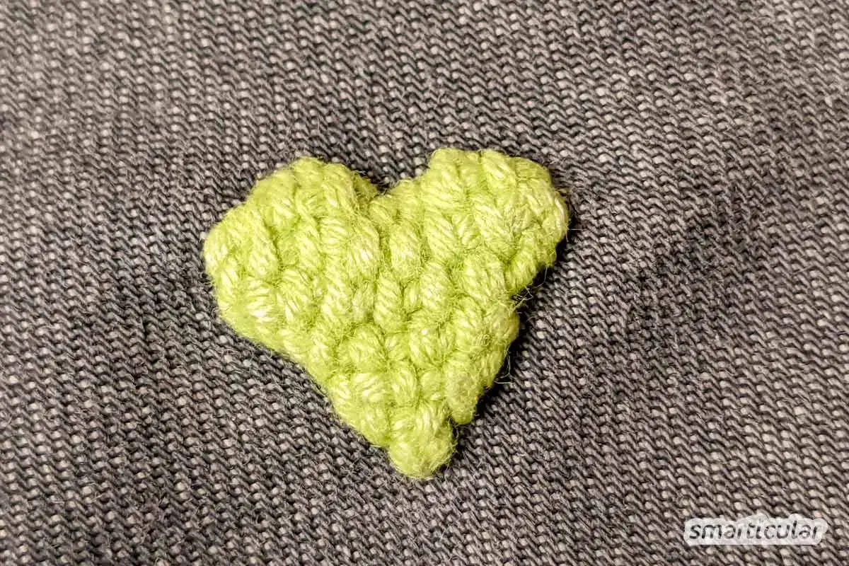 Ein gehäkeltes Herz in leuchtendem Grün bedeckt ein kleines Loch im Stoff. Ein unsichtbarer Flicken, der Liebe zeigt.