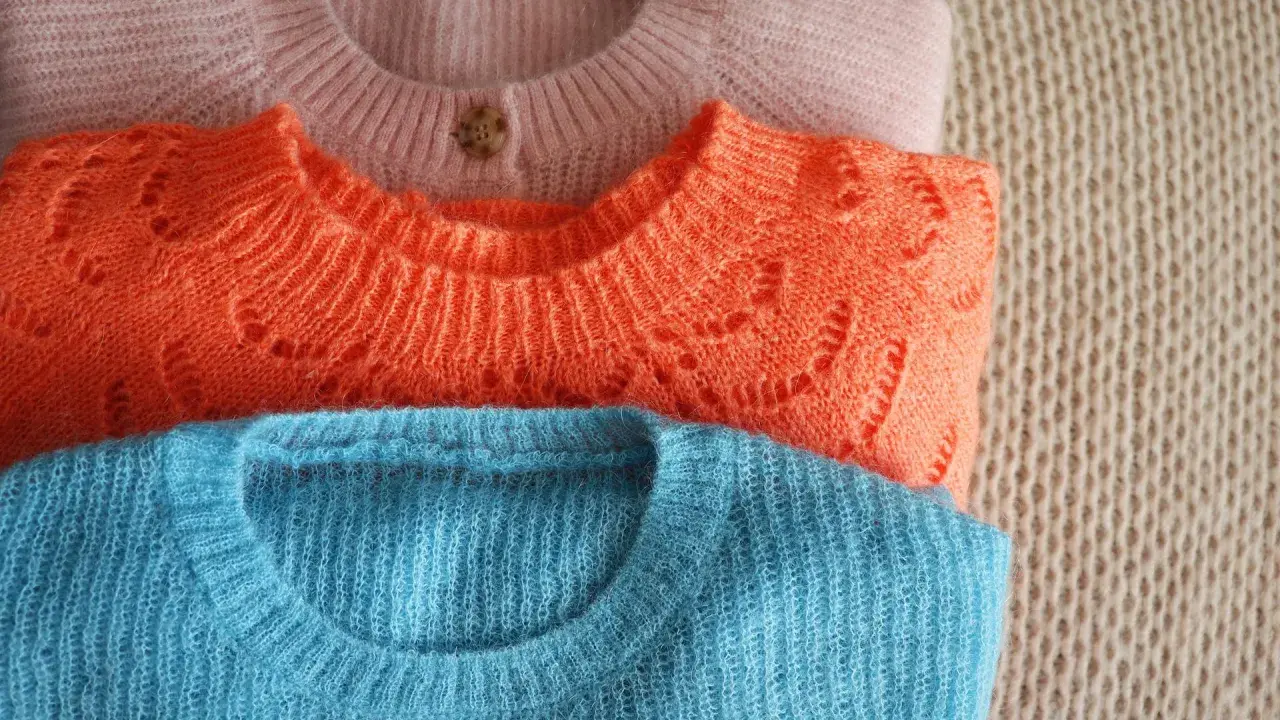 Gestapelte Pullover in Rosa, Orange und Blau. Der Wollprogramm-Waschmaschinen-Zyklus ist ideal für diese feinen Strickwaren.