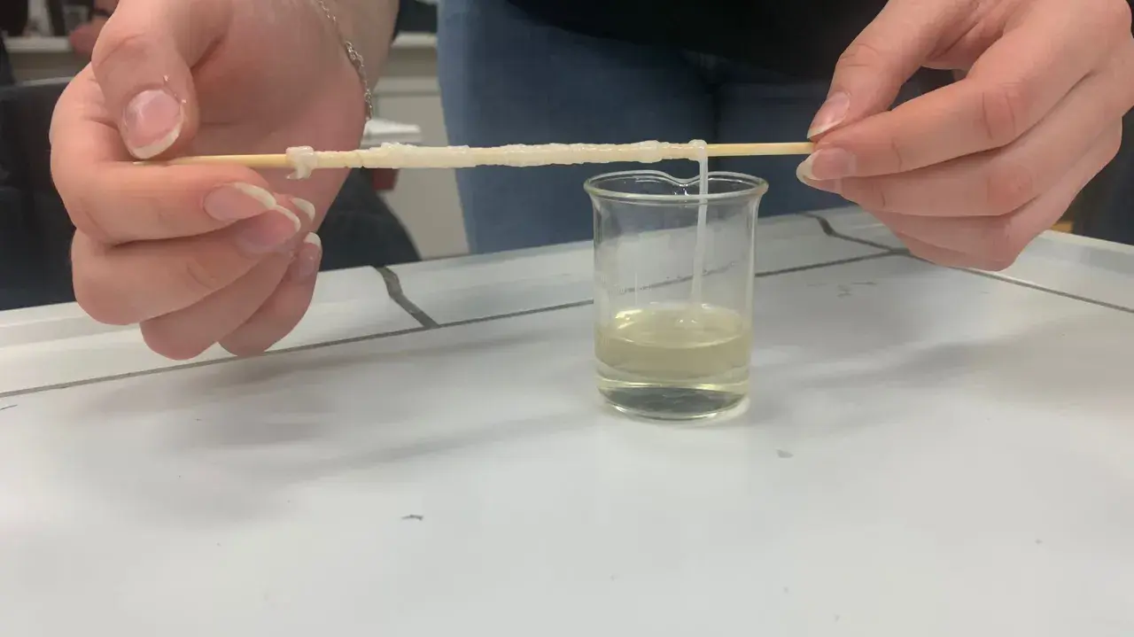 Hände ziehen einen Faden aus einer Flüssigkeit, der zeigt, woraus Nylon besteht.