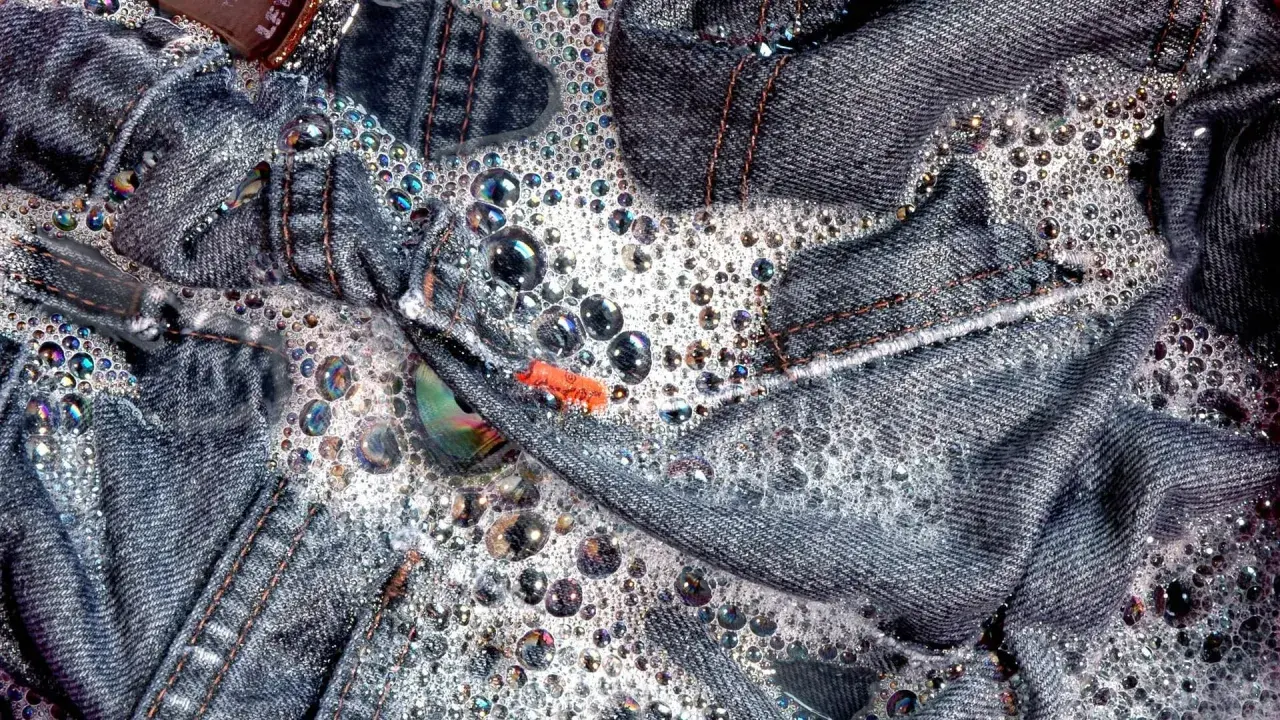 Jeans schleudern in schaumigem Wasser. Bunte Seifenblasen tanzen auf dem Denim.