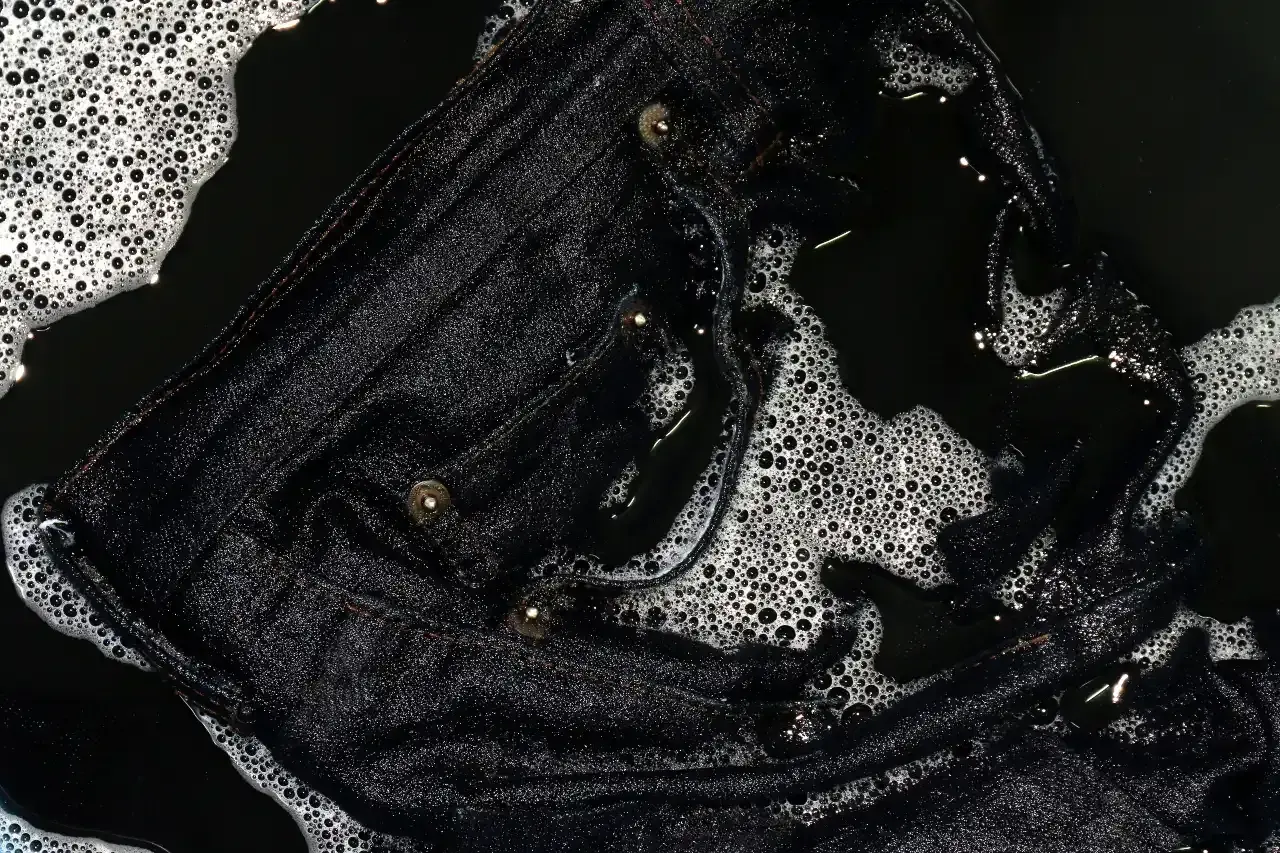 Eine schwarze Hose wird gewaschen. Schaum und Wasser bedecken den Stoff, der gerade gereinigt wird.