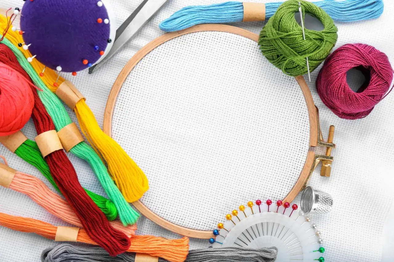 Buntes Stickgarn, Nadeln, Schere, Fingerhut und Stickrahmen – alles, was man zum Sticken braucht, liegt bereit für kreative Projekte.