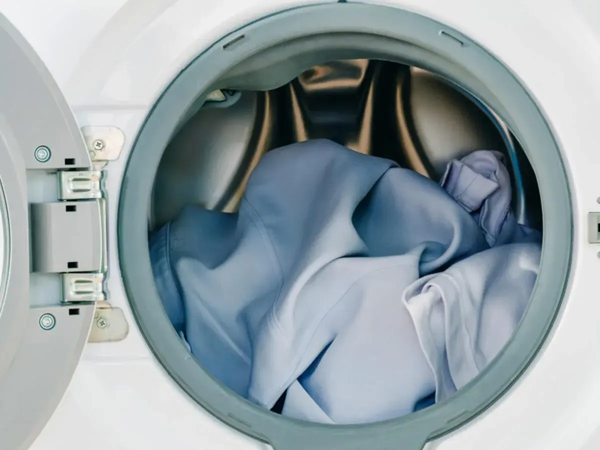 Blaue Kleidung, darunter ein Hemd aus Polyester, wartet im Trommel der Waschmaschine auf den Schleudergang.
