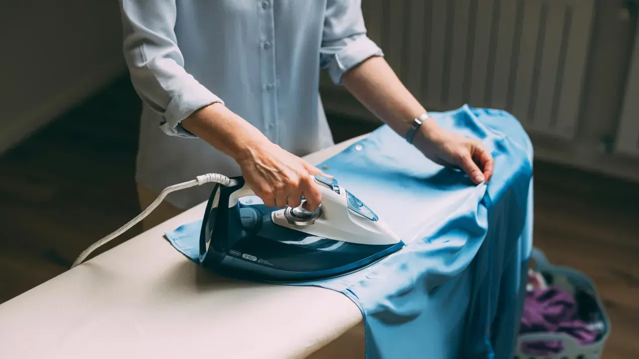 Frau bügelt ein hellblaues Kleid aus knitterfreier Viskose.