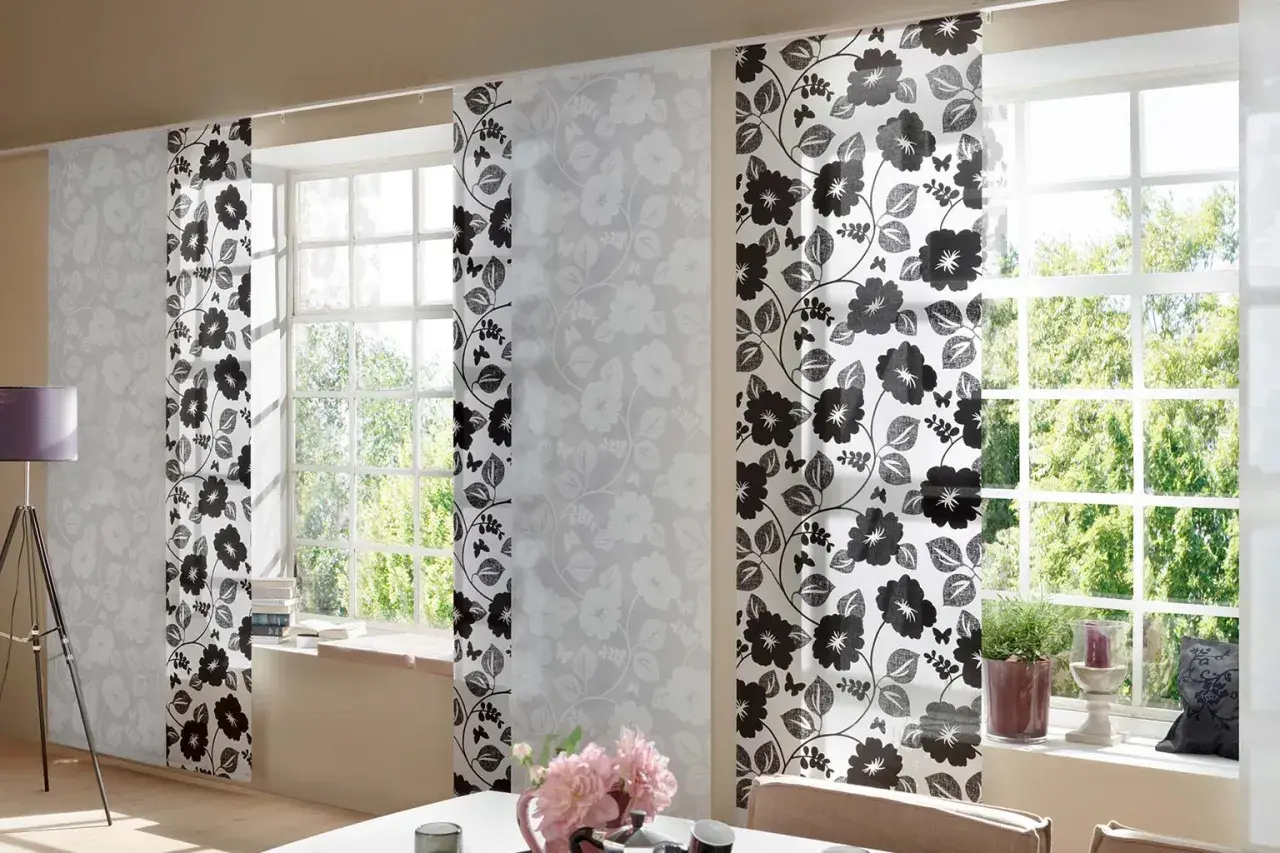 Schiebegardine kurz mit floralem Muster in Schwarz und Weiß. Helle Paneele mit zarten Blüten und dunklere mit kräftigen Blumen und Schmetterlingen schmücken das Fenster.