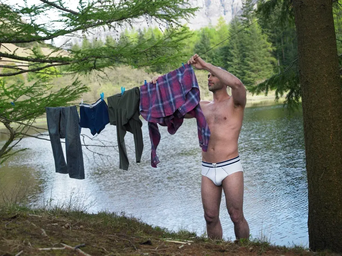 Mann hängt Wäsche auf, darunter auch eine **Boxershorts**, zum Trocknen am Seeufer.