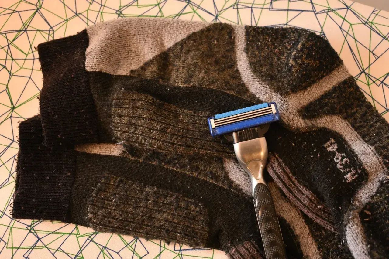 Rasierklinge liegt auf einem stark verknöteltem, gemustertem Schlauch. Pilling hose wird mit der Klinge entfernt.
