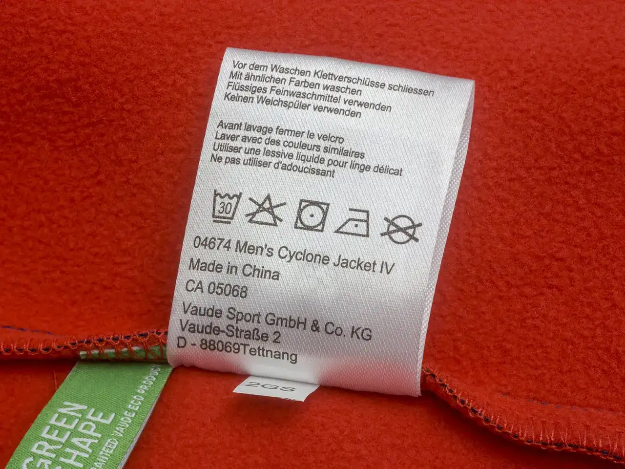 Pflegeetikett einer roten Regenjacke: Klettverschlüsse schließen, mit ähnlichen Farben waschen, Flüssigwaschmittel verwenden.