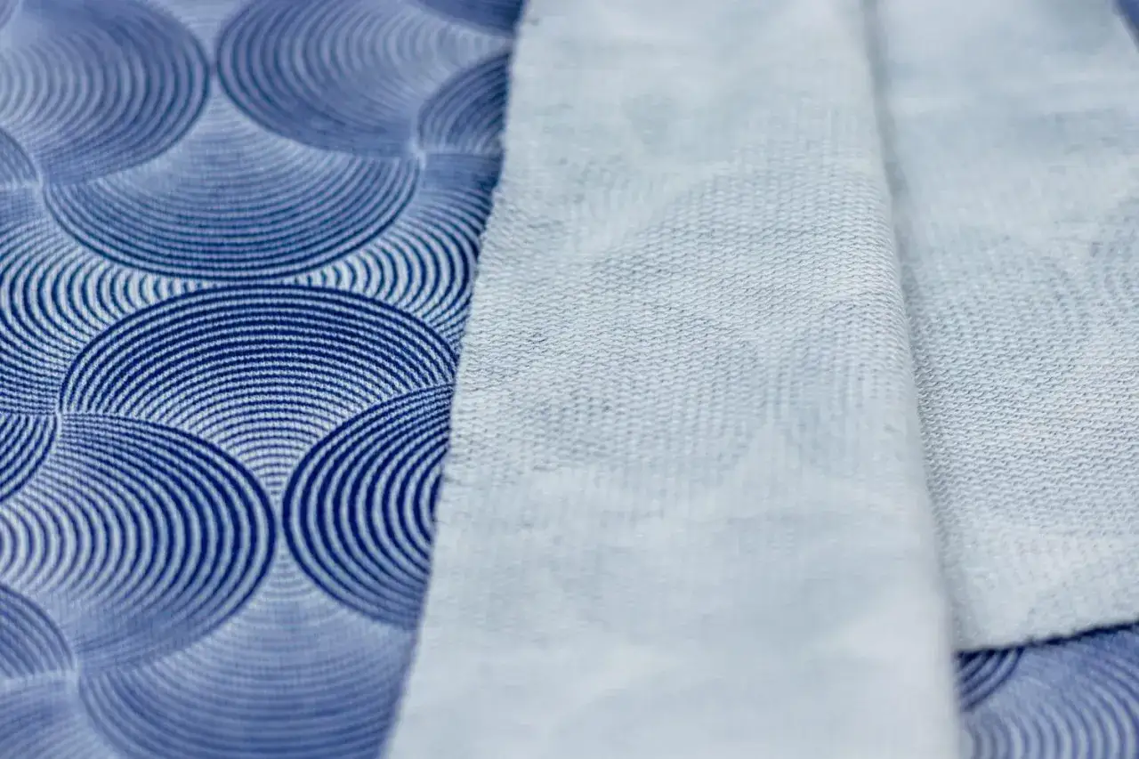 Zwei Stoffe, ein blauer mit Kreismuster, der andere hellblau, liegen nebeneinander. Der hellblaue Stoff ist weich und fühlt sich an, als wäre er bereit für das modal stoff waschen.