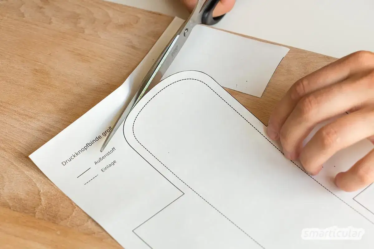 Schere schneidet Schnittmuster für stoffbinden nähen. Ein Hand hält das Papier, während die andere Hand die Schere führt.