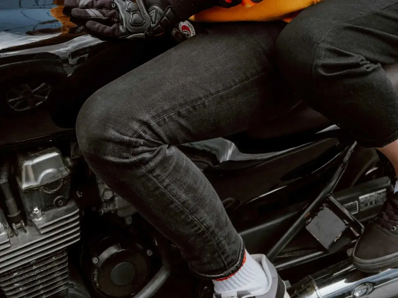 Person sitzt auf einem Motorrad, trägt schwarze Jeans, die frisch gewaschen aussehen, und Motorradhandschuhe.
