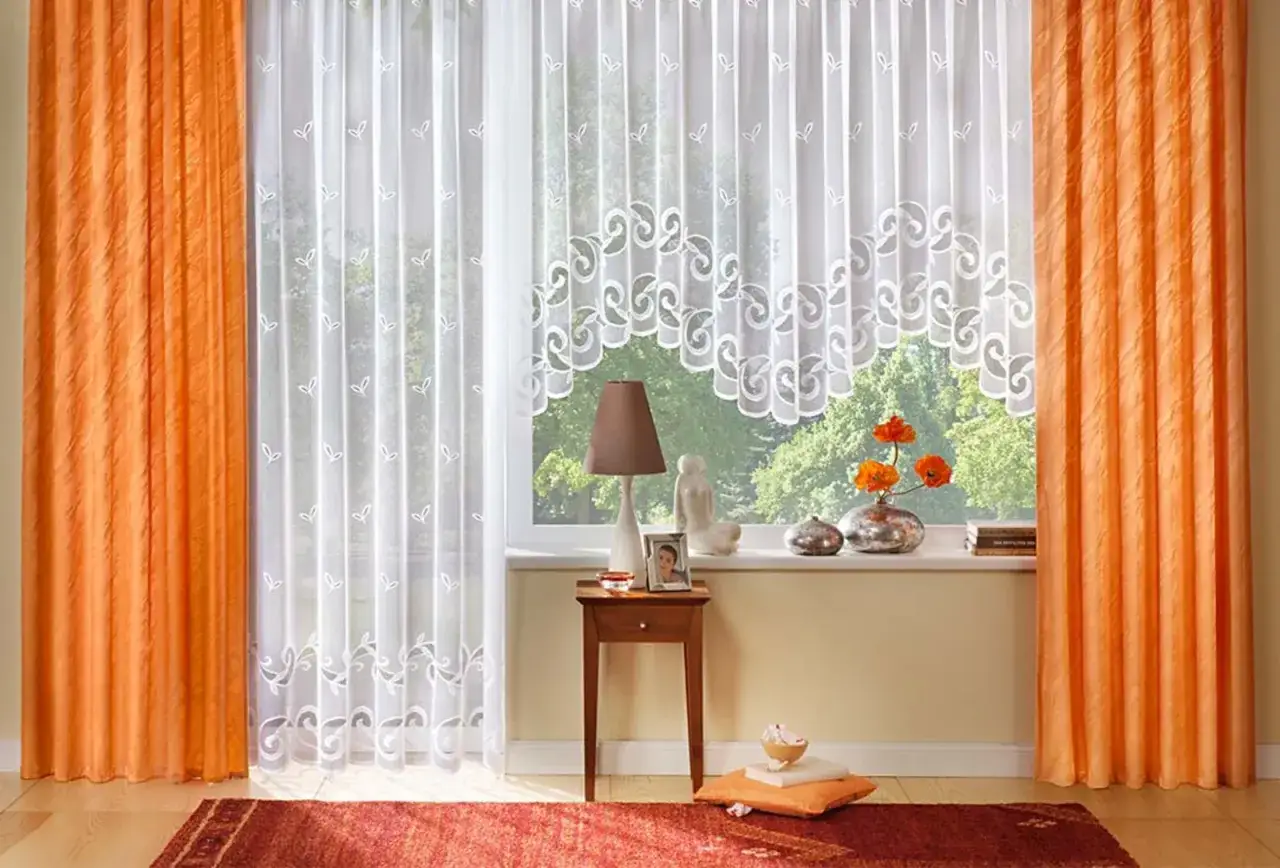 Orange Gardinen rahmen ein Fenster mit zarten weißen Stores, die bis zur Fensterbank reichen.