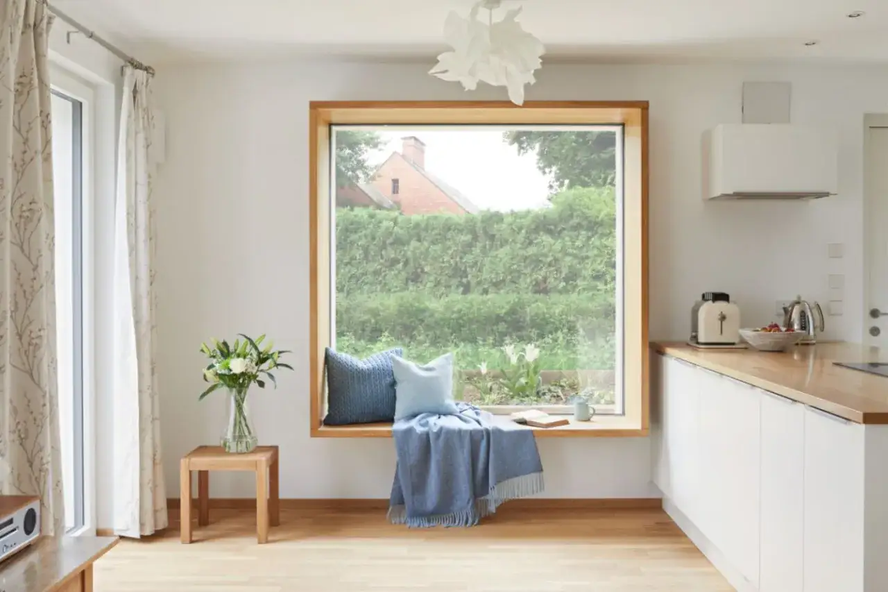 Gemütliche Sitzecke am Fenster ohne Fensterbank: Kissen, Decke und Buch laden zum Verweilen ein.