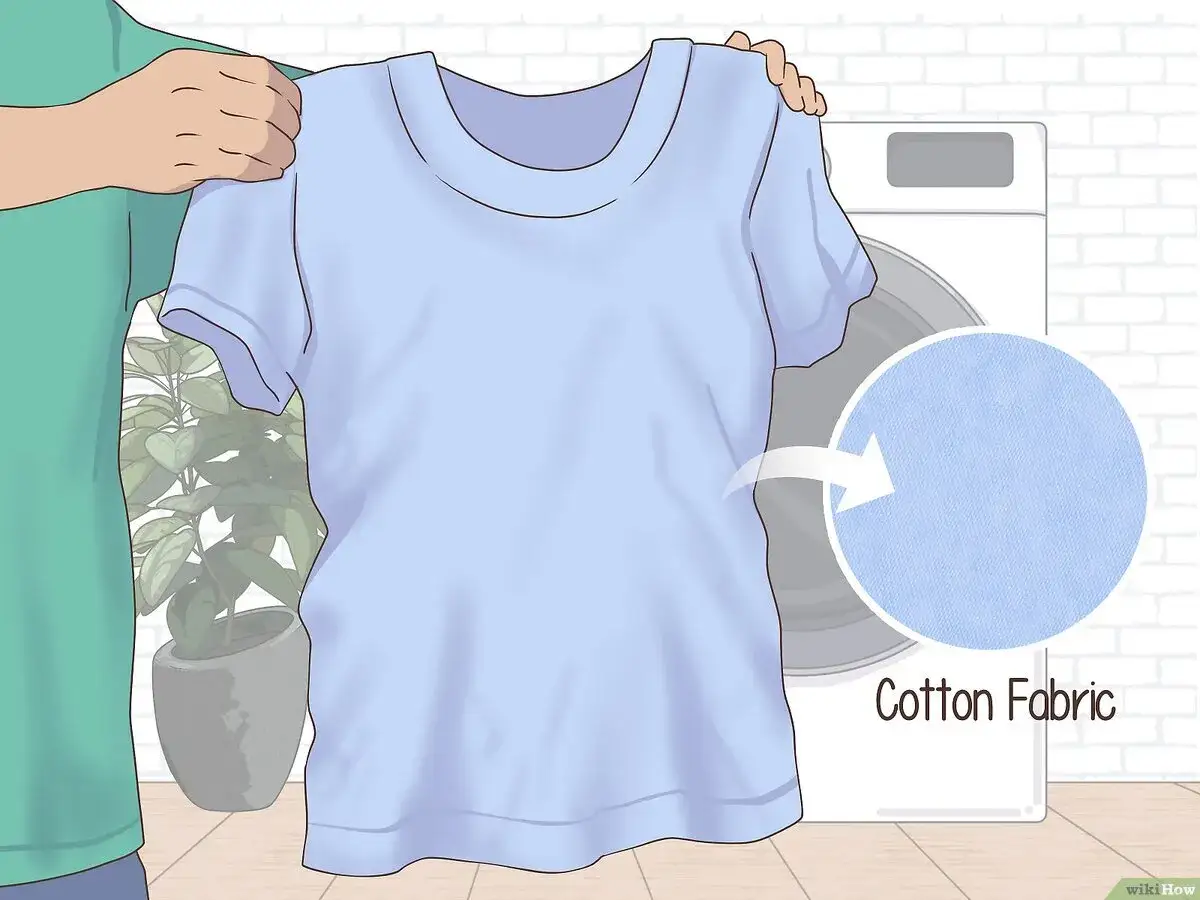 Hilfe, um eingelaufene Kleidung zu retten! Eine Person hält ein hellblaues Baumwoll-T-Shirt vor einer Waschmaschine.