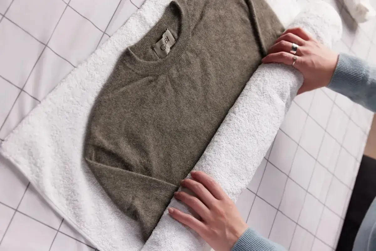 Ein brauner Kaschmirpullover wird auf einem weißen Handtuch ausgebreitet, um ihn nach dem Waschen mit Essig zu trocknen.