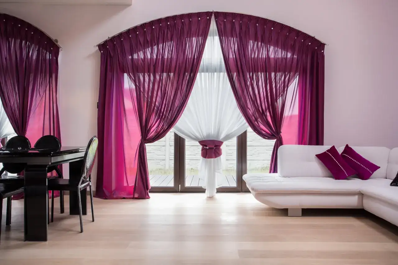 Schiebegardinen kombinieren: Elegante, fließende Stoffe in Lila und Weiß schaffen ein luxuriöses Ambiente vor dem großen Fenster.