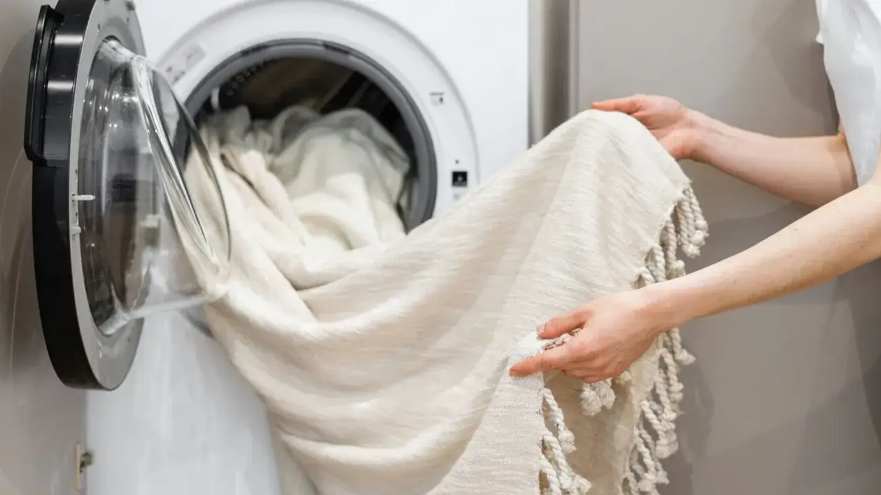 Helle Gardinen werden in die Waschmaschine geladen. Ein Hausmittel wie Backpulver kann helfen, sie wieder strahlend wei&szlig; zu machen.