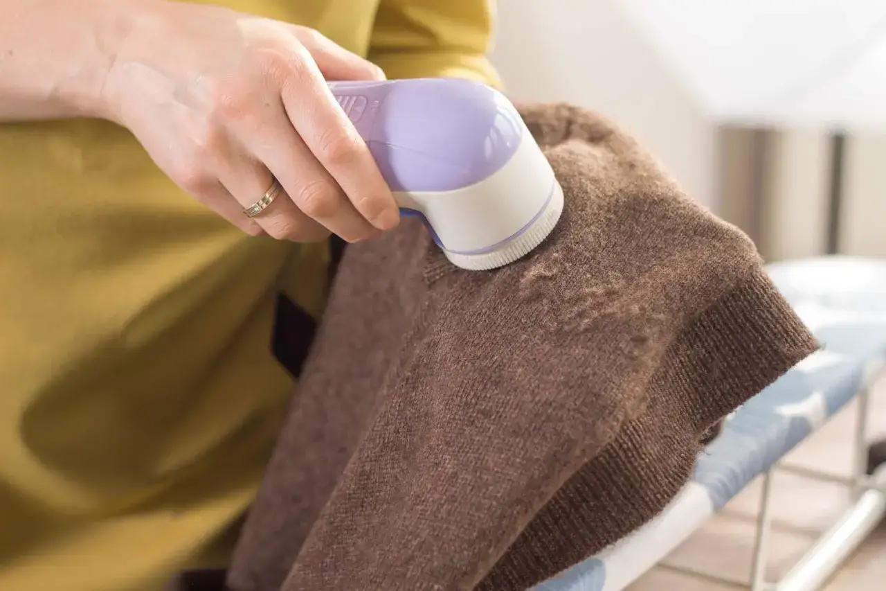 Hand entfernt mit Fusselrasierer lästiges Pilling von einem braunen Pullover.