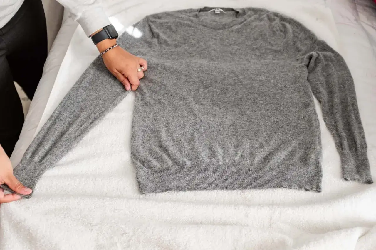 Grauer Kaschmirpullover wird auf einem Handtuch ausgebreitet, bereit zum Kaschmir waschen.