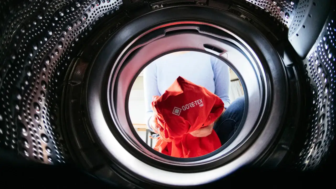 Blick in eine Waschmaschine: Eine Person hält ein rotes Gore-Tex-Jacke. Das Outdoor-Programm ist sinnvoll für solche Kleidung.