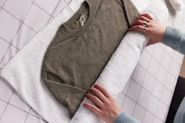 Ein brauner Kaschmirpullover wird auf einem weißen Handtuch gerollt, um ihn nach dem Waschen mit Essig zu trocknen.