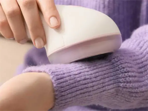 Hand uses a device to remove pilling from a lavender sweater.